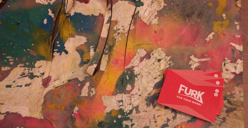 Photo d'un tableau abstrait aux multiples couleurs avec la carte de visite de Furk posée dessus